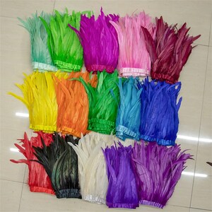 May include: Assortment of feather trim in various colours, including green, pink, purple, blue, yellow, orange, white, black, and red. The feathers are arranged in rows and are approximately 10 inches long.