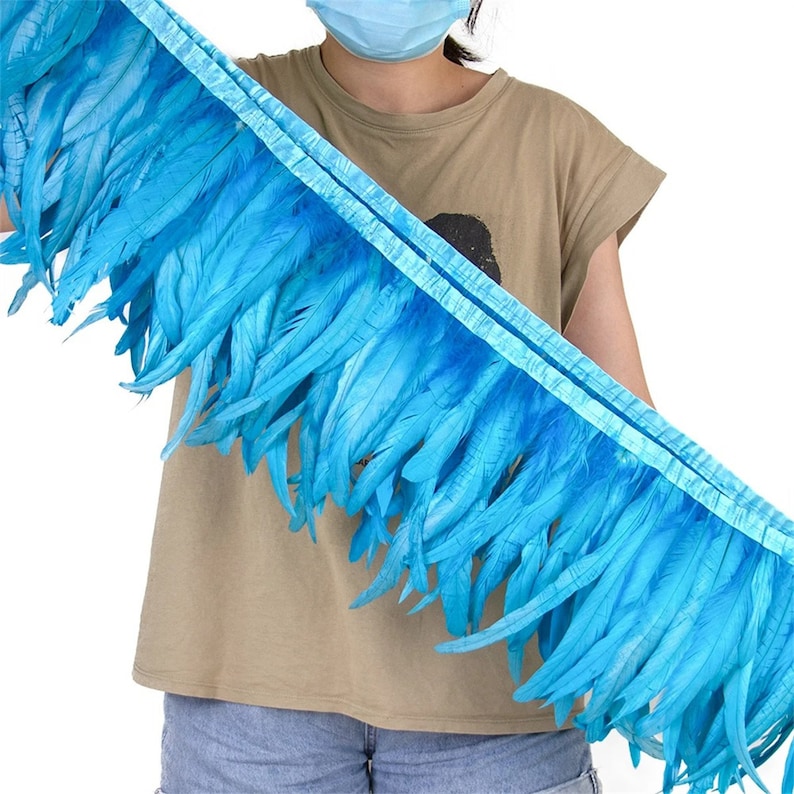 May include: A turquoise blue feather trim with a satin backing. The trim is approximately 15 cm wide and is made of soft, natural feathers.