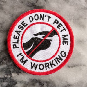 May include: Red and white embroidered patch with the text "Please Don't Pet Me I'm Working" and a black silhouette of a dog with a red line through it.