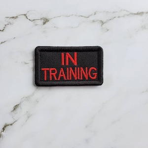 May include: Black embroidered patch with red text that reads "IN TRAINING".