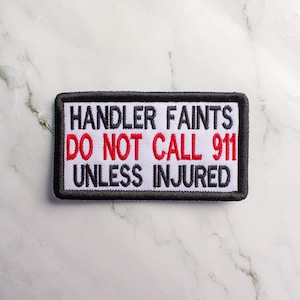 May include: White embroidered patch with black border and red text. The text reads "HANDLER FAINTS DO NOT CALL 911 UNLESS INJURED".