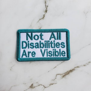 May include: A teal blue embroidered patch with white text that reads "Not All Disabilities Are Visible".