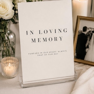 Peut inclure: Un panneau rectangulaire en acrylique transparent portant le texte imprimé en noir IN LOVING MEMORY et le texte plus petit FOREVER IN OUR HEART, ALWAYS PART OF OUR DAY. Le panneau est maintenu verticalement par un socle en acrylique.