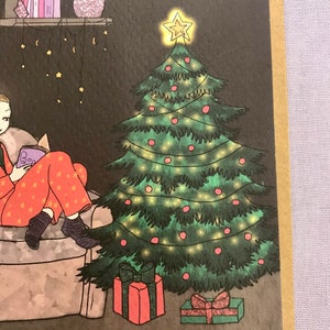 May include: A green Christmas tree with red ornaments and white lights. There are two presents under the tree, one red and one green. The tree is in a room with a person sitting in a chair reading a book.