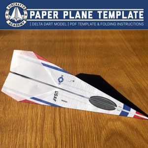 Op de afbeelding: Een papieren vliegtuig sjabloon voor een delta dart model. De sjabloon heeft een witte achtergrond met rode, witte en blauwe strepen, een ster en de tekst "USAF".