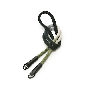 Pode incluir: Uma correia de câmera preta, verde e branca com pontas de couro preto e argolas de metal.