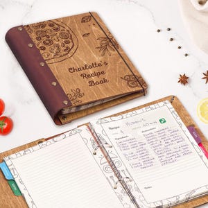 Könnte beinhalten: Hölzernes Rezeptbuch mit einem Pizza-Design und dem Text "Charlotte's Recipe Book". Das offene Buch zeigt ein Hummus-Rezept. Das Buch hat einen dunkelbraunen Rücken und einen Metallringordner.
