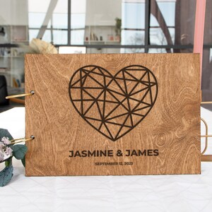 K&ouml;nnte beinhalten: Ein G&auml;stebuch aus Holz mit einem geometrischen Herzdesign und dem Text "Jasmine & James September 12, 2023".
