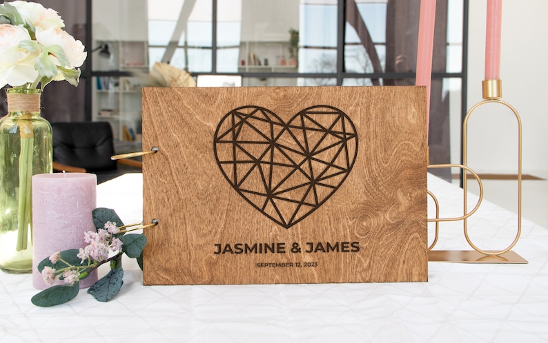 K&ouml;nnte beinhalten: Ein G&auml;stebuch aus Holz mit einem geometrischen Herzdesign und dem Text "Jasmine & James September 12, 2023".