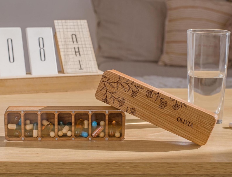 May include: A wooden pill box with seven compartments, filled with various pills. The box is engraved with a floral design and the name "Olivia".