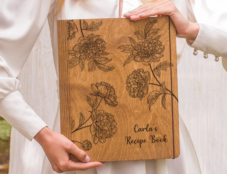 Puede incluir: Un libro de recetas de madera con un dise&ntilde;o floral y el texto "Carla's Recipe Book" grabado en la portada.