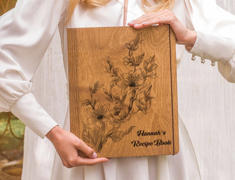 Puede incluir: Un libro de recetas de madera con un dise&ntilde;o floral y el texto "Hannah's Recipe Book" grabado en la portada.