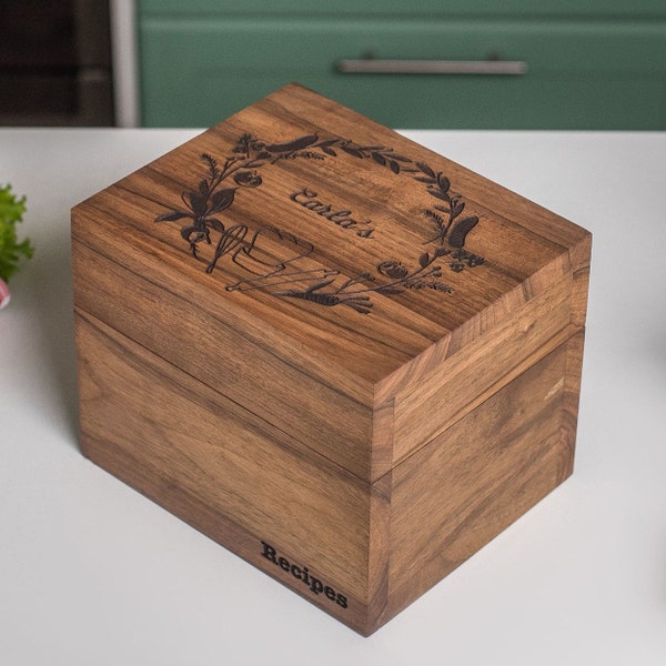 Könnte beinhalten: Eine Holzkisten für Rezepte mit einer dunkelbraunen Beize. Die Oberseite der Kiste ist mit einem gravierten Design eines Kranzes aus Blättern und Gemüse mit dem Text "Earla's" in der Mitte verziert. Die Vorderseite der Kiste ist mit dem Wort "Rezepte" unten graviert.