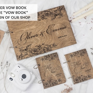 K&ouml;nnte beinhalten: Zwei h&ouml;lzerne Gel&uuml;bdeb&uuml;cher mit Blumendesigns und dem Text "His Vow" und "Her Vow" auf den Deckeln. Ein gr&ouml;&szlig;eres h&ouml;lzernes Gel&uuml;bdebuch mit dem Text "Oliver & Emma" und einem Blumendesign auf dem Deckel.