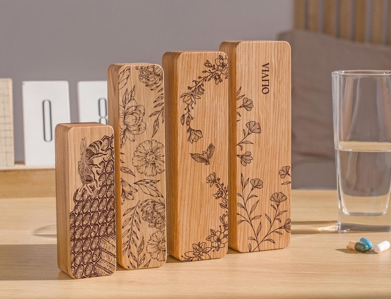 May include: Four wooden boxes with engraved floral designs and the name "Olivia" on one box. The boxes are arranged in a row from left to right, with the largest box on the right and the smallest box on the left.