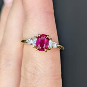 Peut inclure: Une bague en or ornée d'un grand rubis ovale central, flanqué de diamants plus petits, de taille marquise. Le rubis est d'un rouge profond, et les diamants scintillent sur le bandeau en or. Un bijou classique et élégant.
