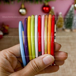 May include: A set of 10 colorful plastic hair bands in various colors, including purple, blue, yellow, green, white, red, pink, gold, orange, and black.