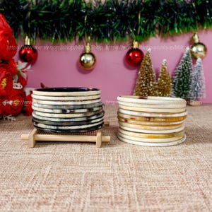 Peut inclure: Deux piles de bracelets en corne, une pile est noire et blanche, l'autre est crème et marron. Les piles sont sur une surface tissée.