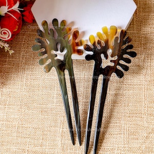 Può includere: Due bastoncini per capelli marroni e neri con un motivo floreale decorativo. I bastoncini sono fatti di corno e hanno una finitura naturale e lucida.
