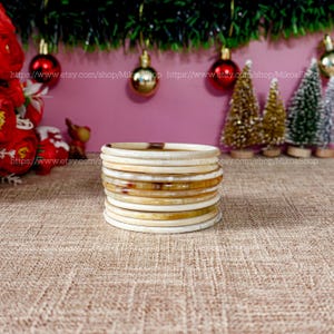 May include: A stack of 12 ivory and brown bangles. The bangles are made of a natural material and have a smooth, polished finish.