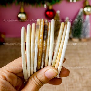 May include: A stack of 10 white and brown horn bangles. The bangles are smooth and polished, and they have a natural, organic look.