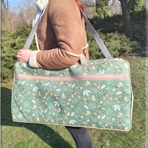 Può includere: Una grande borsa trapuntata verde rettangolare con un motivo floreale, portata a tracolla. La borsa ha una cerniera e finiture beige e una tracolla grigia. Il testo "DiZayCraftStudio" è visibile in basso.