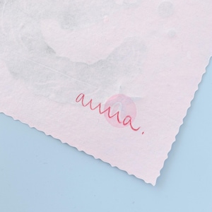 Puede incluir: Una hoja de papel texturizado rosa p&aacute;lido con bordes dentados que presenta un patr&oacute;n abstracto gris tenue y el texto manuscrito en cursiva roja "anna." en la esquina inferior, sobre un fondo azul claro s&oacute;lido.