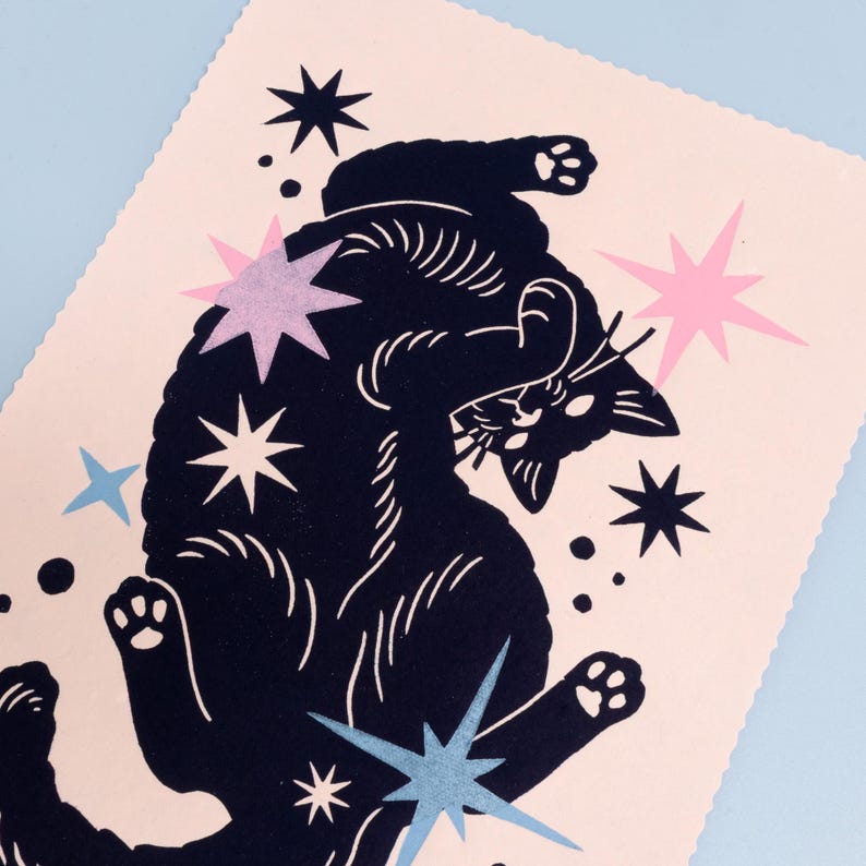 Puede incluir: Una impresi&oacute;n rectangular sobre papel rosa claro que presenta la silueta negra de un gato acostado boca arriba con las patas levantadas. El gato est&aacute; rodeado por varias formas de estrellas en negro, azul claro, lavanda y rosa, junto con peque&ntilde;os puntos negros.
