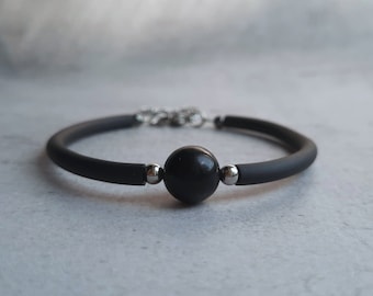 May include: A black silicone bracelet with a single black bead and silver accents.