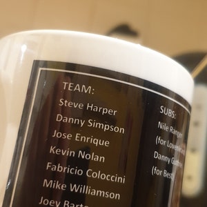 K&ouml;nnte beinhalten: Eine schwarz-wei&szlig;e Tasse mit einer Namensliste. Der Text lautet "TEAM: Steve Harper, Danny Simpson, Jose Enrique, Kevin Nolan, Fabricio Coloccini, Mike Williamson, Joey Barton, Cheick Tiote, Leon Best" und "SUBS: Nile Ranger (f&uuml;r Lovenkrands), Danny Guthrie (f&uuml;r Best)"