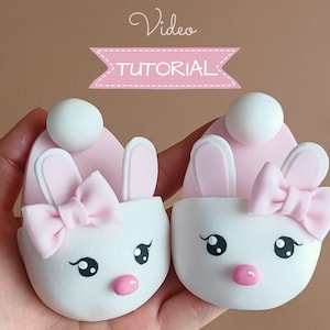 May include: Two pink and white bunny-shaped cake pops with white fondant faces, pink noses, and black eyes. Each cake pop has a pink bow and bunny ears.