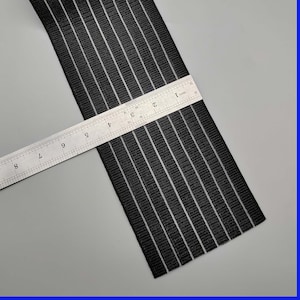 Puede incluir: Banda elástica negra con rayas blancas, medida con una regla que muestra 23 cm de longitud.