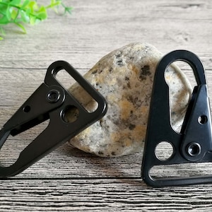 May include: Two black metal clasps with a hook and loop design. The clasps are on a wooden surface.