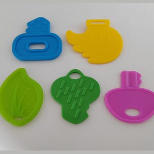 May include: Five colorful plastic shapes: a blue perfume bottle, a yellow banana bunch, a green leaf, a green cloud-like shape, and a pink key. These shapes are likely for a child's toy or educational activity.