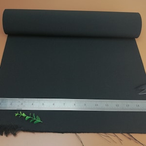 Könnte beinhalten: Schwarzer Stoff mit ausgefransten Kanten. Ein Lineal liegt auf dem Stoff, die Zahlen 1 bis 16 sind sichtbar. Eine kleine grüne Pflanze befindet sich im Vordergrund.