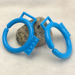 Puede incluir: Dos anillos de plástico azul brillante con un asa en cada uno. Los anillos están diseñados para sujetar objetos juntos.