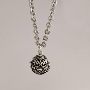 May include: A silver chain necklace with a silver charm pendant. The charm is a round, openwork design with a floral pattern.