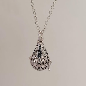 Op de afbeelding: Een zilveren ketting met een zwarte en witte bejeweled hanger. De hanger heeft de vorm van een traan en heeft een ingewikkeld ontwerp.