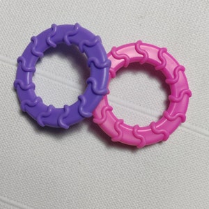 May include: Two plastic rings, one purple and one pink, with a wavy design. The rings are interlocked.