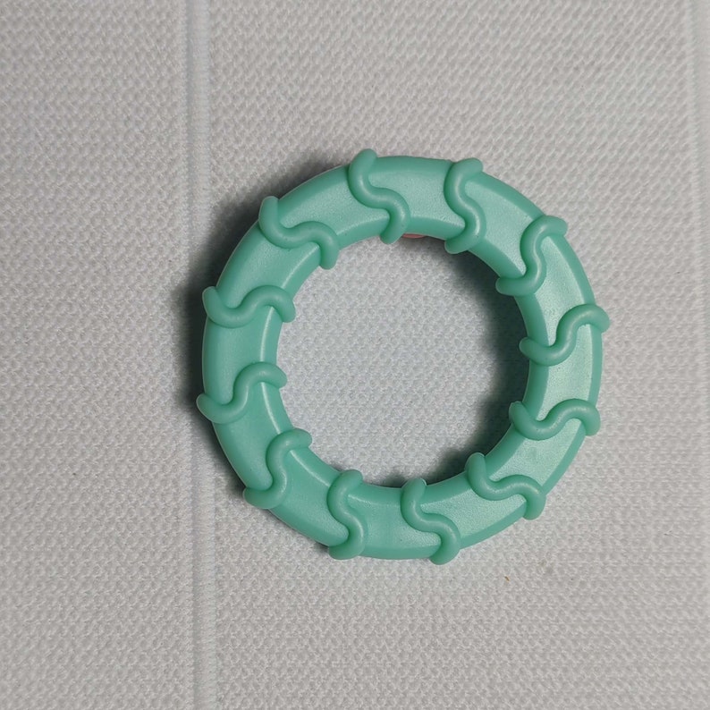 May include: A turquoise blue plastic ring with a wavy design. The ring is about 2 inches in diameter.