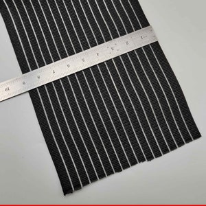 Puede incluir: Banda elástica de rayas blancas y negras con una regla que mide 25,4 cm.