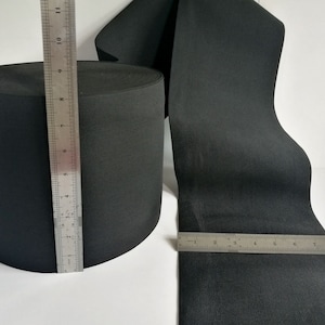 Op de afbeelding: Zwarte elastische band opgerold naast een liniaal die 28 cm meet. De elastische band is 2,5 cm breed.