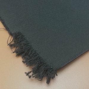 May include: A close-up of a dark gray fabric with a frayed edge. The fabric has a textured, woven appearance.