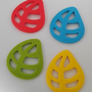 May include: Four colorful leaf-shaped silicone trivets. The trivets are in red, blue, green, and yellow. Each trivet has a cutout leaf vein design. These trivets are designed to protect surfaces from heat.