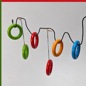 May include: A set of colourful wooden rings hanging from a black wire. The rings are green, red, orange, and blue.