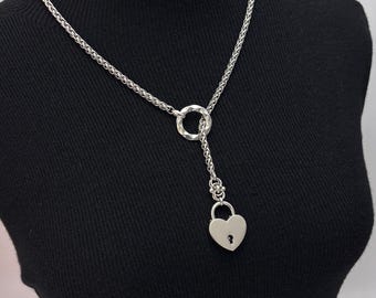 May include: Silver-toned necklace featuring a heart-shaped padlock pendant. The necklace has a textured chain and a circular accent. The pendant hangs from a delicate chain, creating a stylish and unique accessory.