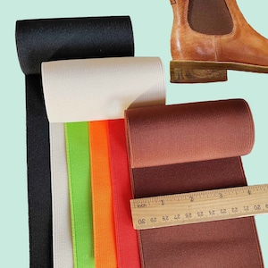 Peut inclure: Cinq rouleaux de tissu &eacute;lastique en noir, blanc, vert, orange et marron. Le tissu est c&ocirc;tel&eacute; et a un l&eacute;ger brillant. Une r&egrave;gle est plac&eacute;e sur le tissu marron, montrant des mesures en pouces.
