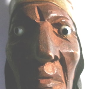 May include: A carved wooden bust of a Native American man. The sculpture is detailed with visible facial features, including eyes, nose, and mouth. The bust is primarily brown with lighter accents on the headdress.