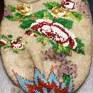 May include: A drawstring pouch crafted from beige fabric, densely covered in intricate glass beadwork. The design features floral motifs in red, white, yellow, and green, with a prominent blue and orange geometric pattern at the base and a beaded tassel.