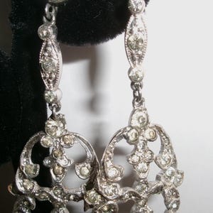 Puede incluir: Un letrero de madera rústico blanco con la palabra "Welcome" en un estilo manuscrito. El letrero tiene un aspecto envejecido y un elemento floral decorativo. El fondo es una textura de madera borrosa.